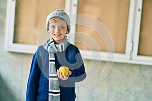 Adorable blond student kid smiling happy holding green apple at the school