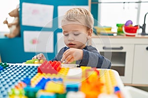 Adorable blond toddler playing with construction blocks sitting on table at kindergarten