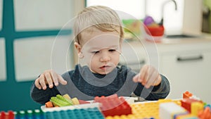 Adorable blond toddler playing with construction blocks sitting on table at kindergarten