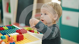 Adorable blond toddler playing with construction blocks sitting on table at kindergarten