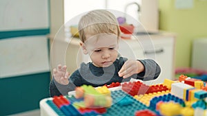 Adorable blond toddler playing with construction blocks sitting on table at kindergarten