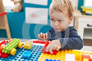 Adorable blond toddler playing with construction blocks sitting on table at kindergarten