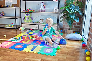 Adorable blond toddler playing using vintage phone around lots of toys at kindergarten