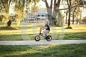 Adorable blonde Australian kid riding a small bicycle in the park