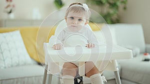Adorable blonde baby smiling confident sitting on highchair at home