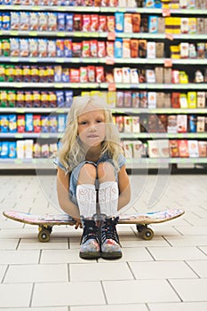 adorable blonde child sitting on skateboard in supermarket