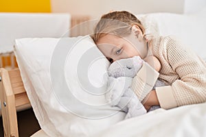 Adorable blonde girl hugging rabbit doll lying on bed at bedroom