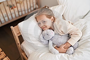 Adorable blonde girl hugging rabbit doll lying on bed at bedroom