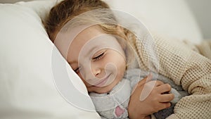 Adorable blonde girl hugging rabbit doll lying on bed at bedroom