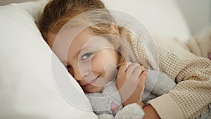 Adorable blonde girl hugging rabbit doll lying on bed at bedroom