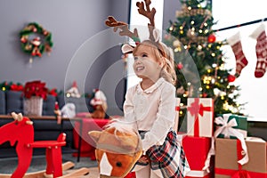 Adorable blonde girl playing with horse toy standing by christmas tree at home