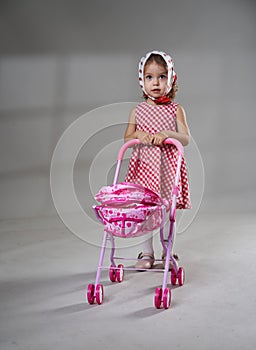 Adorable blonde little girl on gray background, with a baby carriage toy