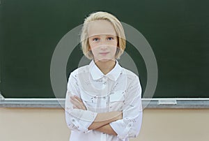 Adorable blonde schoolgirl 9-11 years old in a classroom near a chalkboard. Back to school.
