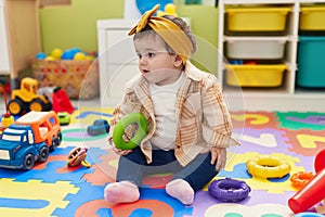 Adorable blonde toddler sitting on floor holding hoop toy at kindergarten