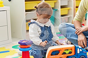 Adorable blonde toddler sitting on floor playing with truck at kindergarten