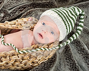 Adorable blue eyed newborn in a knit basket with a green and white knit cap