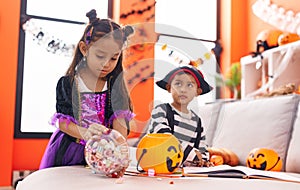 Adorable boy and girl having halloween party holding candies at home