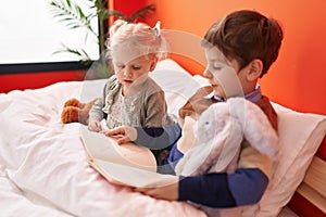 Adorable boy and girl reading book sitting on bed at bedroom