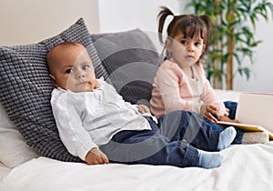 Adorable boy and girl reading book sitting on bed at bedroom