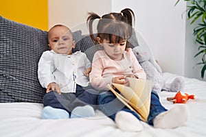 Adorable boy and girl reading book sitting on bed at bedroom