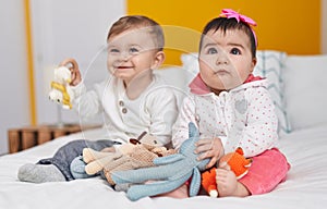 Adorable boy and girl sitting on bed playing with toys at bedroom