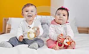 Adorable boy and girl sitting on bed playing with toys at bedroom