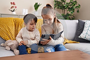 Adorable boy and girl using touchpad sitting on sofa at home