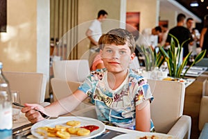 Adorable boy having breakfast at resort restaurant. Happy school kid child eating healthy food, vegetables and eggs in