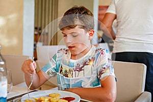 Adorable boy having breakfast at resort restaurant. Happy school kid child eating healthy food, vegetables and eggs in