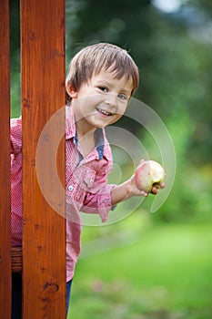 Adorable boy, holding apple, standing next to a door