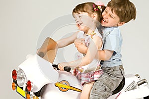 Adorable boy and little girl sitting on toy bike