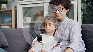 Adorable boy and mother young woman watching TV and talking at home on sofa