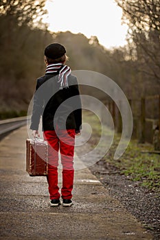 Adorable boy on a railway station, waiting for the train with suitcase