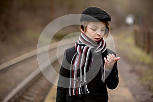 Adorable boy on a railway station, waiting for the train with suitcase