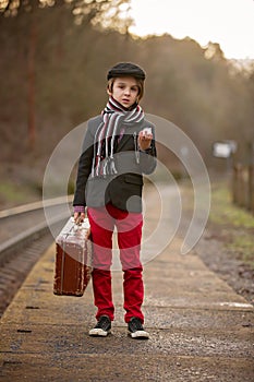 Adorable boy on a railway station, waiting for the train with suitcase