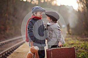 Adorable boy on a railway station, waiting for the train with suitcase and teddy bear