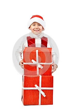 Adorable boy in santa clothes peeks out behind Christmas big gift boxs. Isolated white background.