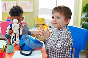 Adorable boys playing telephone and robot toy sitting on table at kindergarten
