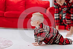 Adorable caucasian baby boy is sitting and holding gift toy Santa Claus near a Christmas tree, many festive gift boxed