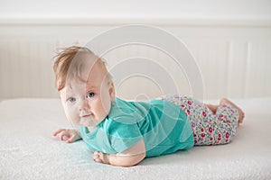 Adorable Caucasian baby girl with blue eyes trying to stand up and walk, looking at the camera calmly with a smile