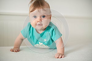 Adorable Caucasian baby girl with blue eyes trying to stand up and walk, looking at the camera calmly with a smile