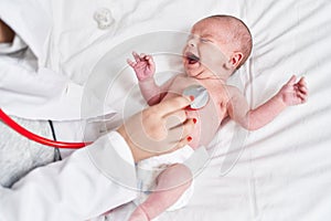 Adorable caucasian baby having heart examination with stethoscope crying at bedroom