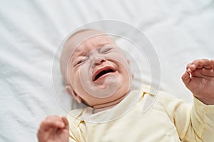 Adorable caucasian baby lying on bed crying at bedroom