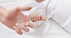 Adorable caucasian baby lying on bed holding mother finger at bedroom