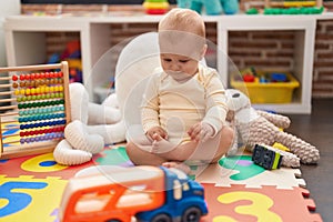 Adorable caucasian baby playing with car and truck toy sitting on floor at kindergarten