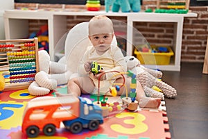 Adorable caucasian baby playing with car and truck toy sitting on floor at kindergarten