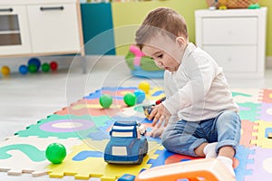 Adorable caucasian baby playing with truck toy sitting on floor at kindergarten