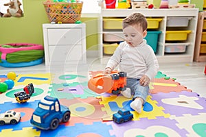 Adorable caucasian baby playing with truck toy sitting on floor at kindergarten