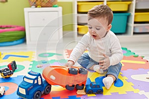 Adorable caucasian baby playing with truck toy sitting on floor at kindergarten