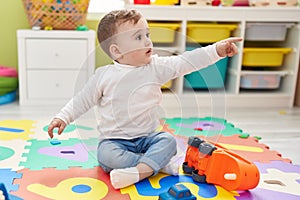 Adorable caucasian baby playing with truck toy sitting on floor at kindergarten